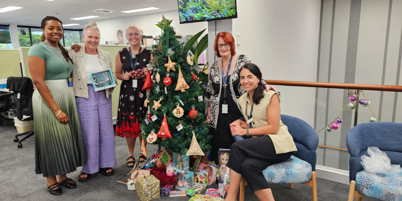 The Gold Coast Domestic and Family Violence Services team gather around the Christmas tree with gifts for women impacted by domestic or family violence.