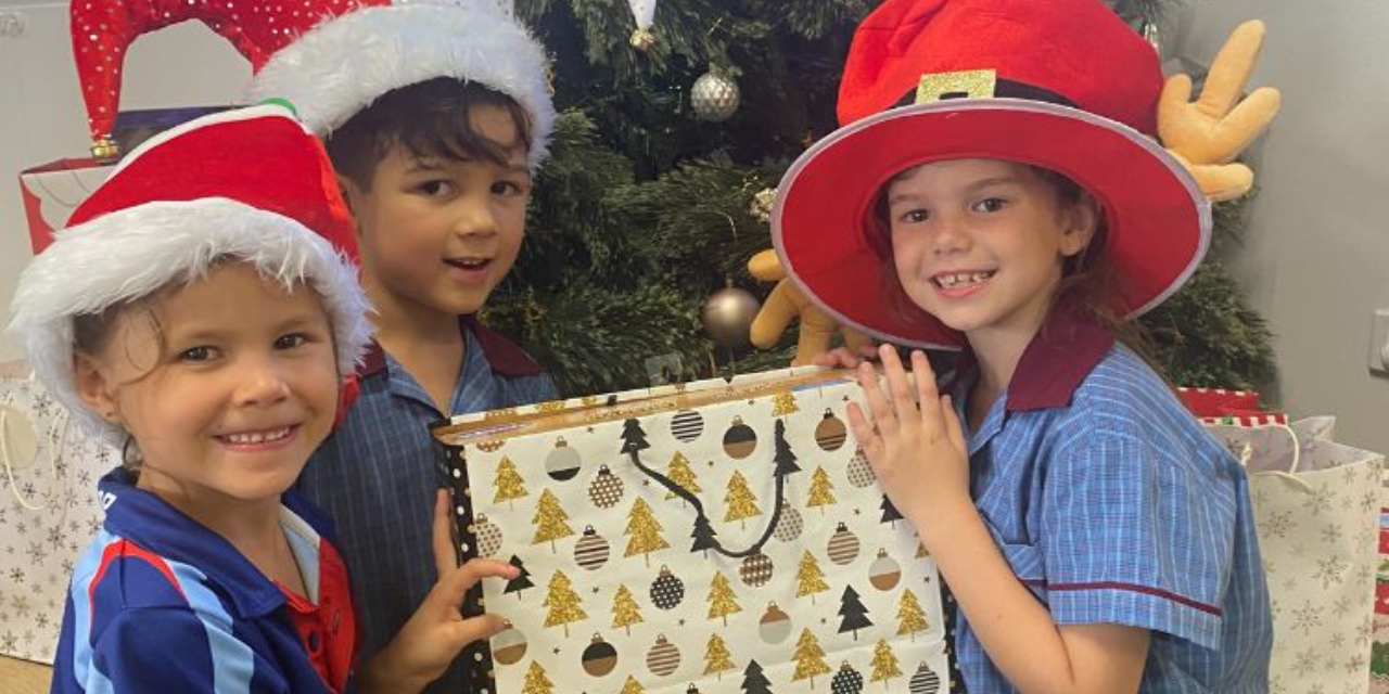 Children from St Bernardine's OSHC place gifts under the Christmas tree for children who will be spending time in Logan Hospital this Christmas.